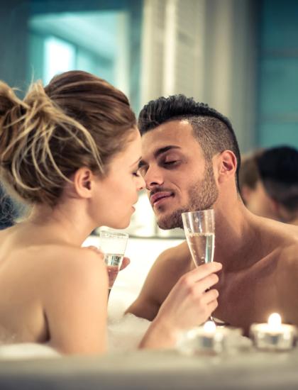 Coppia romantica in vasca da bagno, brindando con champagne.