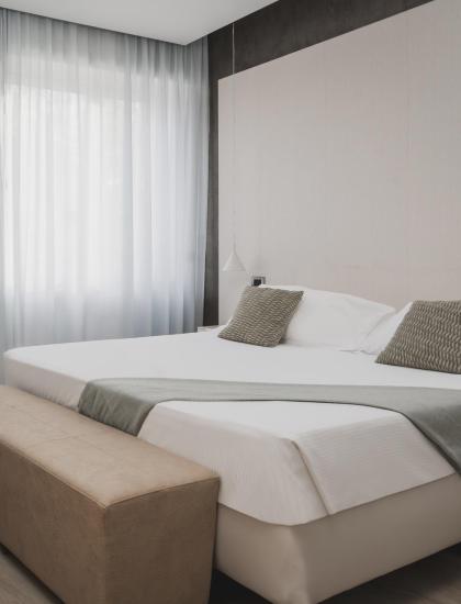 Camera moderna con letto matrimoniale, arredamento minimalista e tende trasparenti.