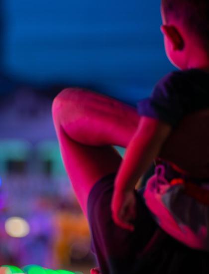 Bambino in braccio, luci colorate sfocate sullo sfondo.