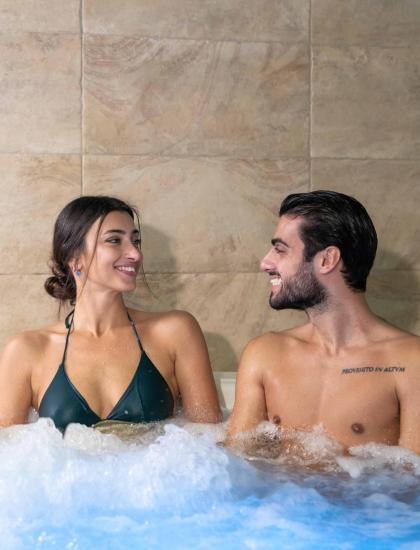 Coppia sorridente in idromassaggio, atmosfera intima e rilassante.