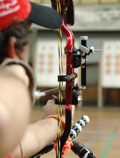 Arcere mira il bersaglio con arco compound in palestra.