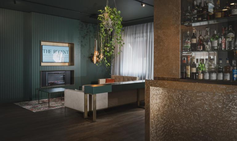 Lounge moderna con bar, divano, piante sospese e camino.