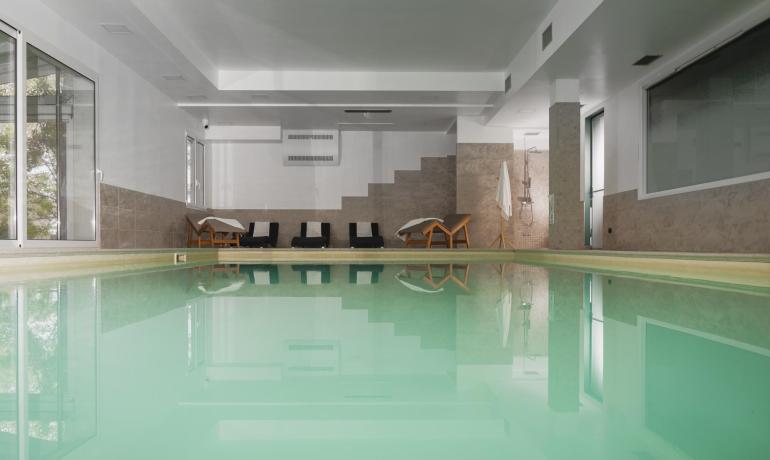 Piscine intérieure avec chaises longues et douche, ambiance relaxante.