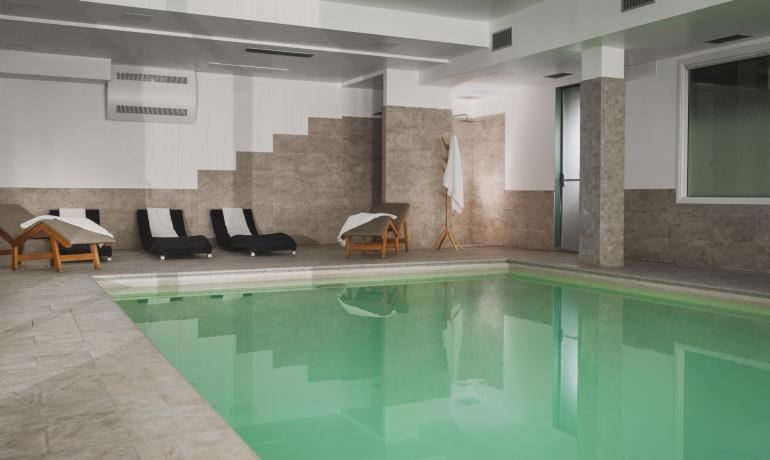 Piscina interna con lettini e pareti piastrellate.
