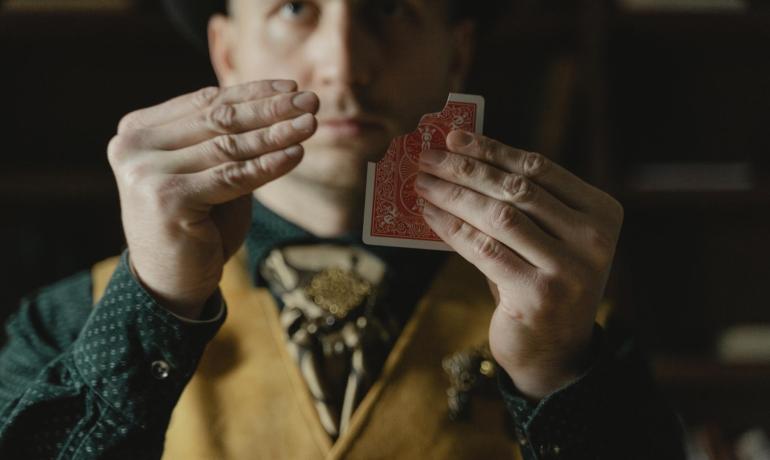 Uomo che esegue un trucco di magia con una carta da gioco.