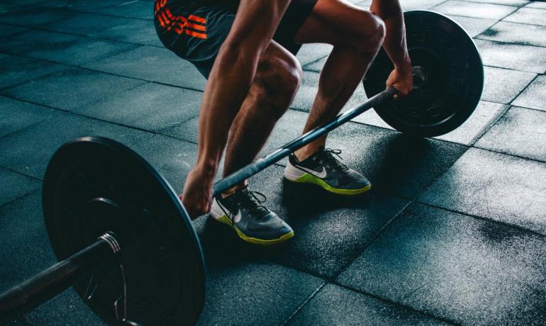 Persona solleva pesi in palestra su pavimento gommato.