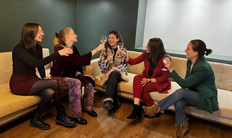 Cinque donne brindano insieme su un divano beige.