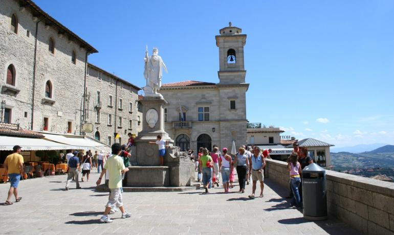 Piazza con statua e persone, cielo sereno.