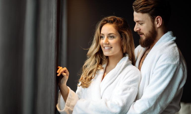 A happy couple in bathrobes looks out the window.