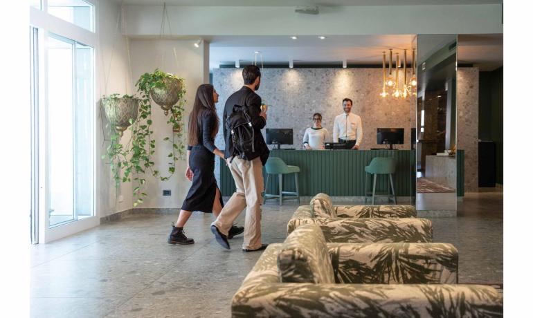 Coppia entra in hotel, accolta dal personale alla reception.