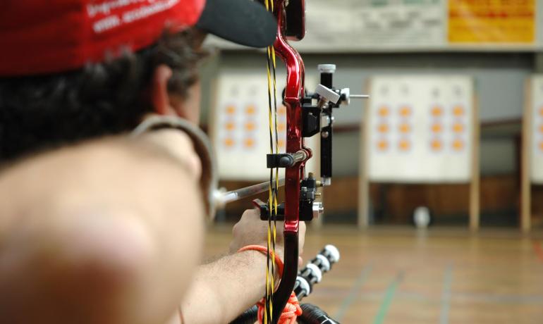 Bogenschütze zielt mit Compoundbogen auf Ziel in der Halle.