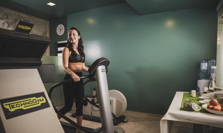 Donna su tapis roulant in palestra con snack sul tavolo.