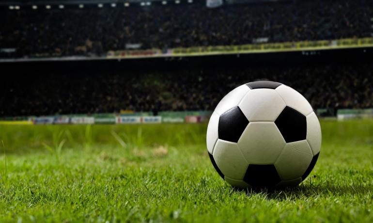 Soccer ball on green field, crowded stadium in background.